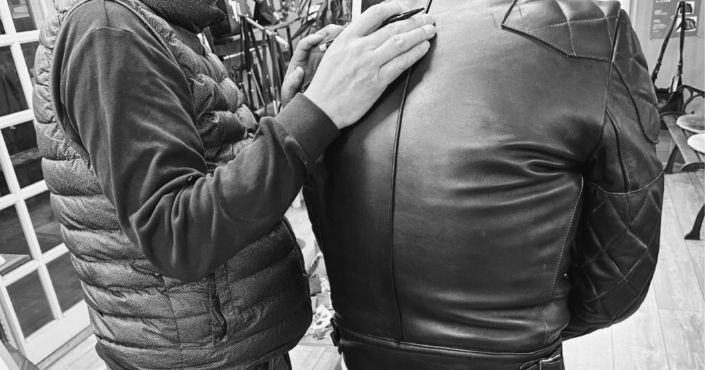サイズアップを希望するお客様に対して、職人がレザージャケットの背中を確認しているご相談風景。