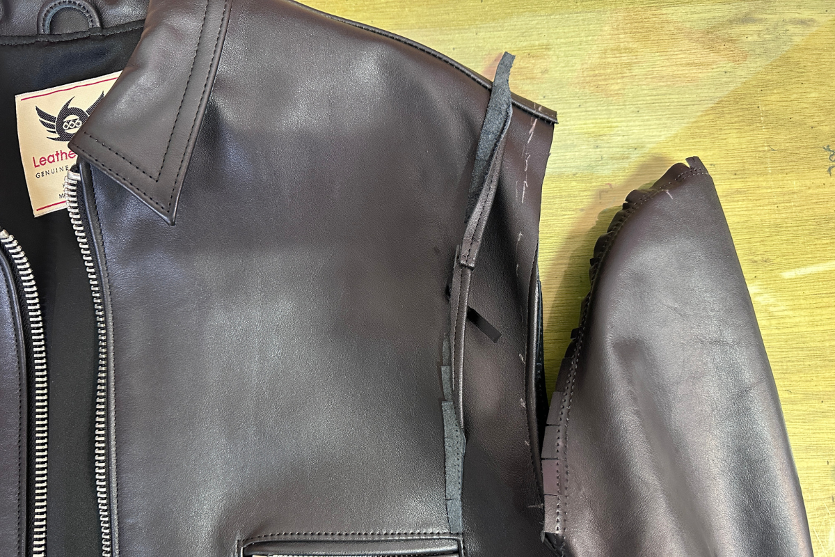肩幅を詰めるために余分な革をカットしたレザージャケットの作業工程 レザージャケットの肩幅を詰める作業中。肩の縫い目を解き、余分な革をカットした状態