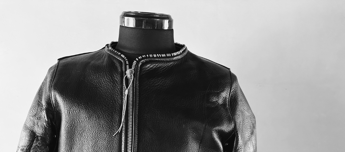 シボ感のあるブラックレザーを使用したノーカラー(襟なし)ライダースジャケット。ミニマルで都会的なデザインが特徴。